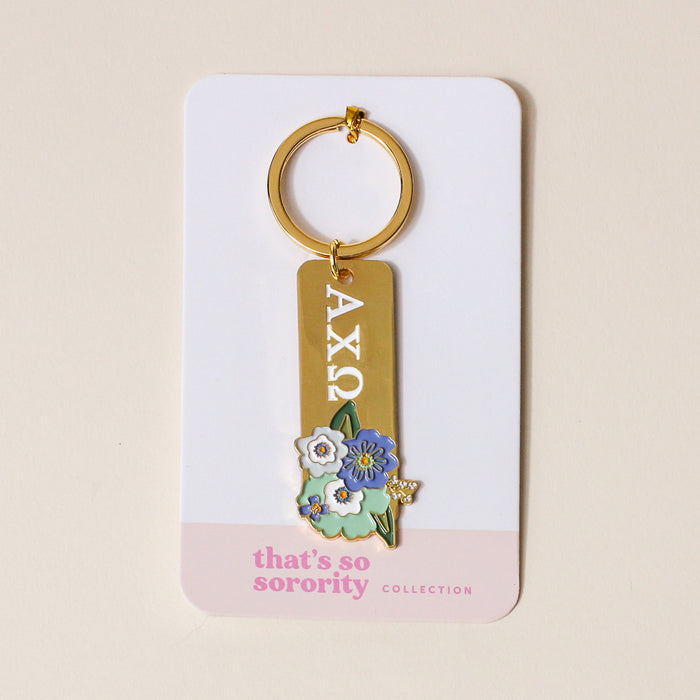 The Darling Effect Alpha Chi Omega Enamel Keychain features gold plating, AXΩ Greek letters, and a blue-and-white flower charm on a “thats so sorority COLLECTION” card—an ideal gift for any Alpha Chi Omega sister.