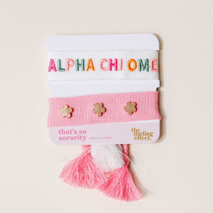 The Darling Effect Alpha Chi Omega Woven Bracelet Set features a white bracelet with ALPHA CHI OMEGA in colorful letters and a pink band with gold flower studs, pink/white tassels—an ideal sorority gift.