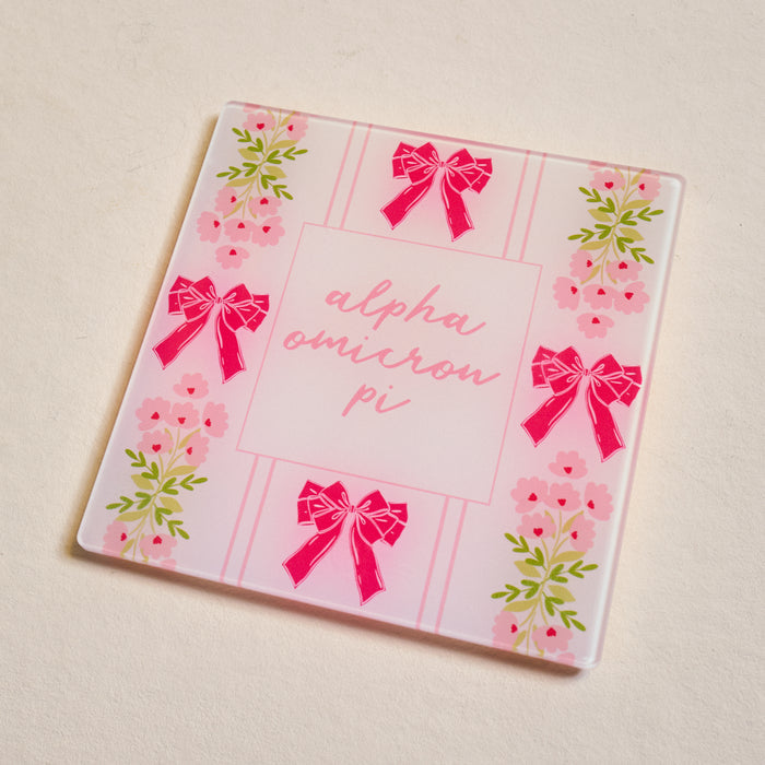 The Darling Effect’s Alpha Omicron Pi Acrylic Coaster features pink bows, florals, and “alpha omicron pi” in cursive—an adorable Big/Little gift for any sorority sister.