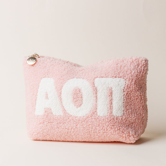 The Darling Effect Alpha Omicron Pi Blush Teddy Letter Pouch features light pink sherpa, a zipper with a round metallic pull, and bold white ΑΟΠ letters—ideal as a carry-on accessory. Set against an off-white background.