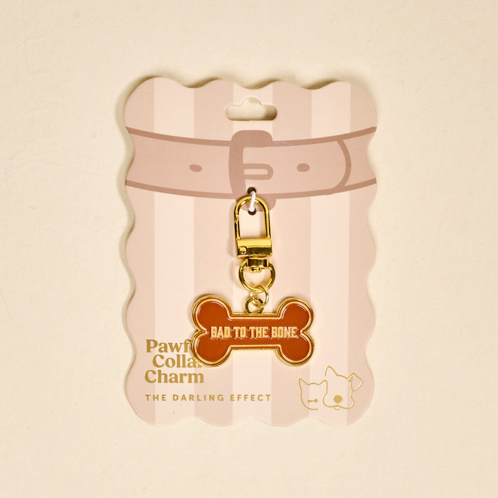 The Darling Effect’s Bad to the Bone Pawfect Collar Charm features a brown bone shape with gold trim and "BAD TO THE BONE" text, attached to gold hardware and displayed on a pink and white card with collar, cat, and dog icons.