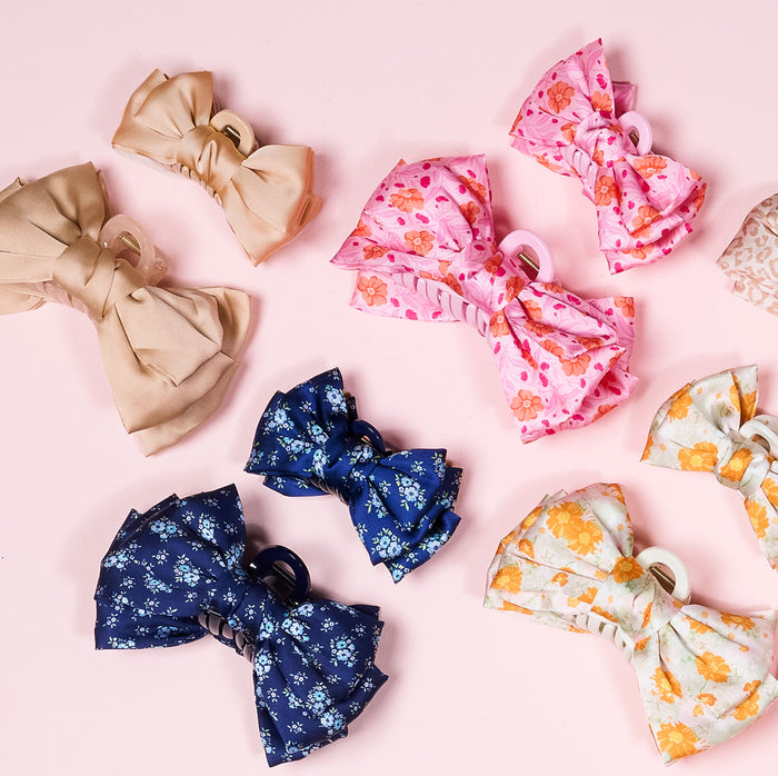 The Darling Effect’s Blush Mini Satin Bow Claw Clip offers a chic touch with its satin bow design, perfect for stylish hairdos. Available in solid beige, pink floral, navy floral, and light green floral prints.