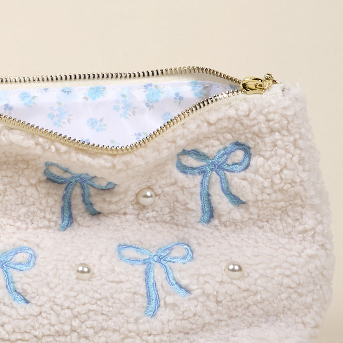 The Bows Blue Teddy Pouch by the-darling-effect features cream sherpa fabric, blue embroidered bows, pearl accents, a gold zipper, and a white floral lining—ideal for mixing and matching with your favorite teddy pouches or accessories.