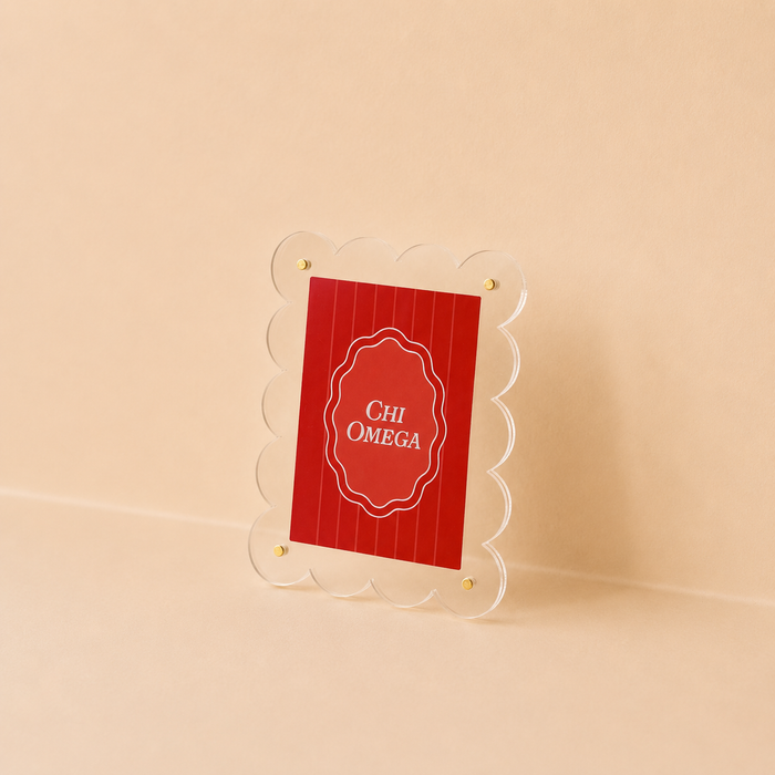 The Darling Effect Chi Omega Mini Acrylic Picture Frame Magnet features a clear, scalloped-edge frame holding a red vertical-striped card with "CHI OMEGA" in white, set on a neutral beige background.