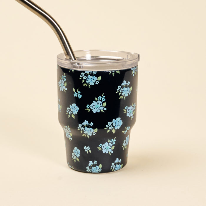 The Dainty Floral Navy 2 oz Tiny Tumbler by the-darling-effect is a black insulated tumbler with a blue floral design and silver metal straw—perfect for keeping your drink at the right temperature on the go.