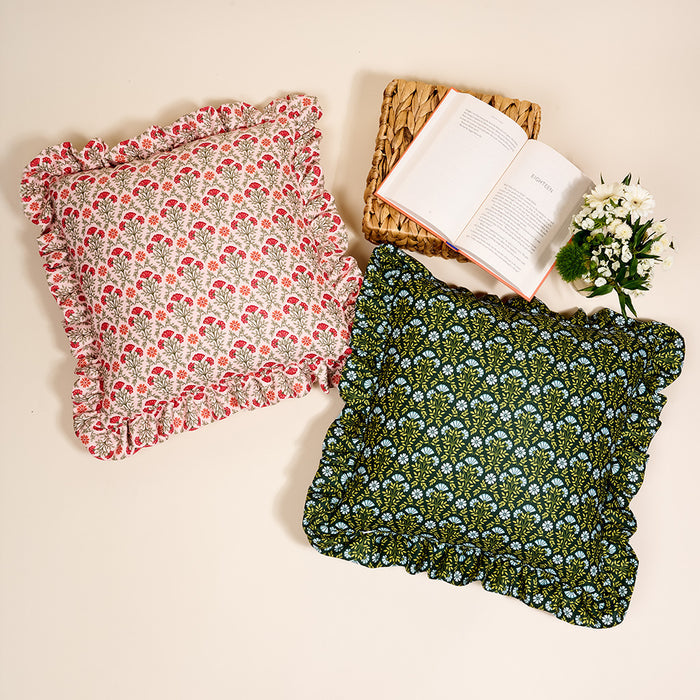 The Darling Effect’s Everbloom Dusty Rose Scalloped Square Throw Pillow, with ruffled edges and floral patterns, sits beside an open book on a woven placemat, creating a charming decorative accent.