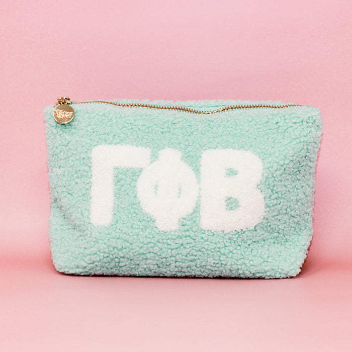 The Darling Effect’s Gamma Phi Beta Aqua Teddy Letter Pouch features fuzzy light blue fabric, white ΓΦΒ letters, and a gold charm zipper—perfect as a cute sorority carry-on accessory.
