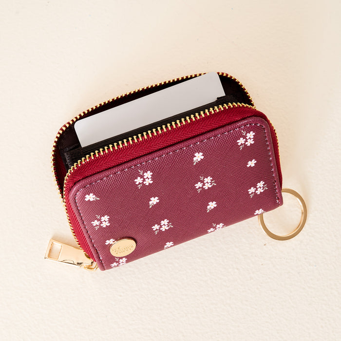 The Darling Effect’s Pretty Posies Plum Zip Around Wallet features a floral pattern, gold zipper, keychain ring, card slots for easy organization, and includes a blank card.