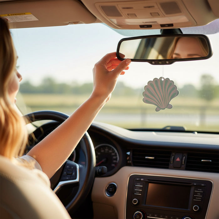 A woman drives, adjusting The Darling Effect’s Seashell Sweet Ride Car Air Freshener on her mirror. Sunlight streams in, filling the car with a unique, long-lasting aroma as the scenery blurs past.