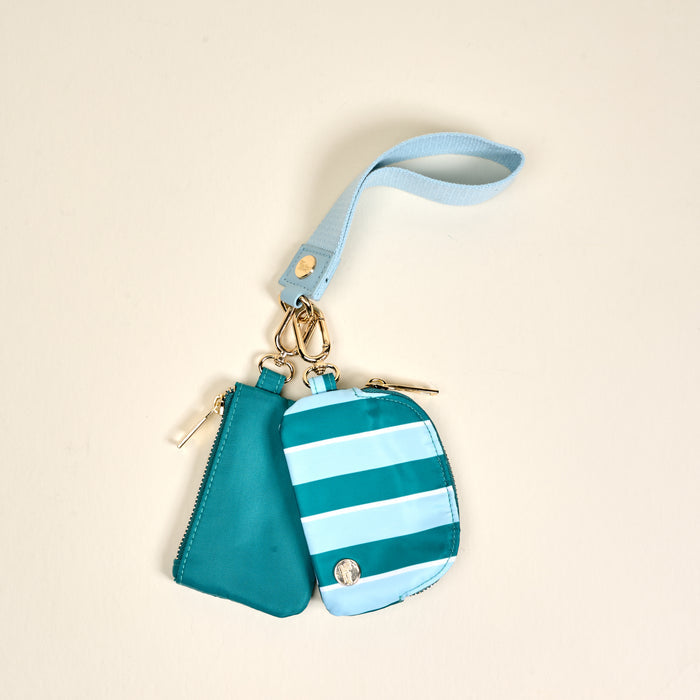 The Darling Effect's Sicily Stripes Teal Dynamic Duo Pouch Wristlet features a luxe gold clasp and includes two pouches—one solid teal, one striped in light and dark blue—set against a plain beige background.
