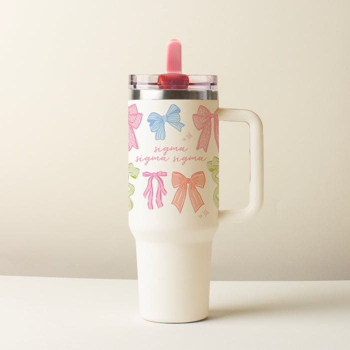The Darling Effect Sigma Sigma Sigma 40 oz Lifestyle Flip Straw Tumbler Bow Affair features a white cup with a handle, colorful bows, “sigma” in pink script, and a pink flip straw lid, displayed on a light surface with a plain background.