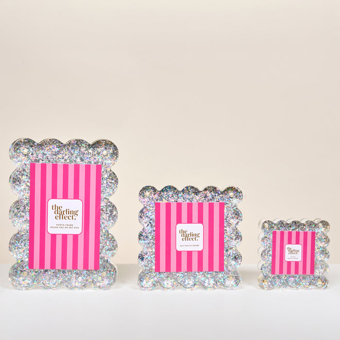 Three Silver Glitter Square Scalloped Acrylic Picture Frames by The Darling Effect, each with a modern design and magnetized panels, are displayed against a neutral background with pink and white striped placeholders featuring the brand logo.