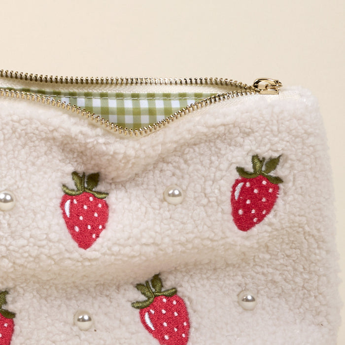 The Darling Effect’s Strawberries & Pearls Teddy Pouch features cream-colored sherpa fabric, embroidered strawberries, pearl accents, and a green gingham lining—an adorable accessory for any collection.