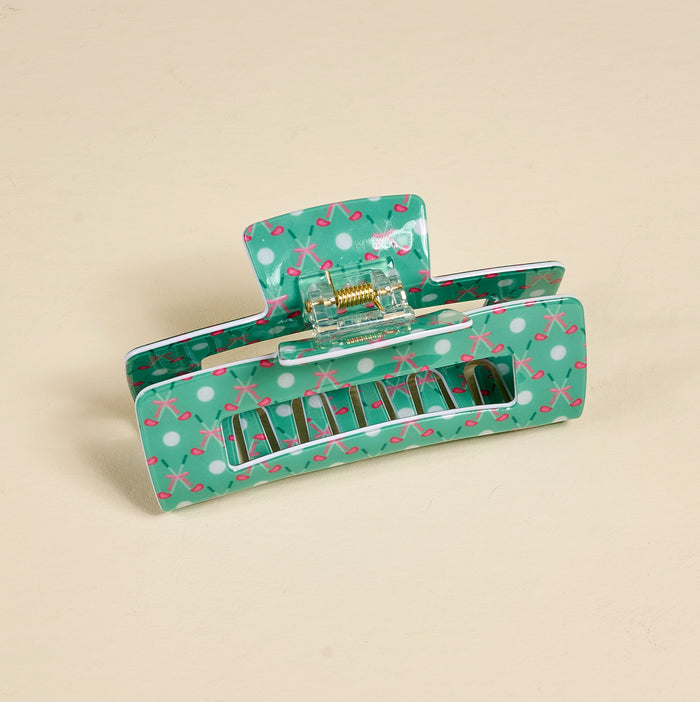 The Darling Effect’s Tee Time Claw Clip features a teal base with white polka dots and pink crisscross lines, delivering a playful look and strong hold for your hair. Shown on a beige background, this accessory is both stylish and practical.
