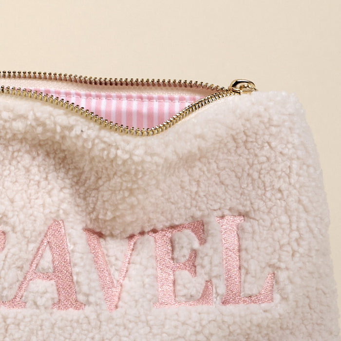 The Darling Effect’s Travel Edit Teddy Pouch is a cream sherpa pouch with pink "TRAVEL" embroidery and a gold zipper, perfect for adding cozy style to your accessories.