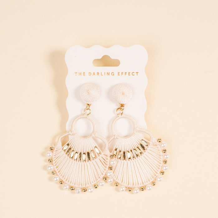 The Darling Effect White Paloma Drop Earrings showcase a fan-shaped woven design with pearl-like beads and gold accents, displayed on a branded card—stylish, lightweight statement earrings against a light beige background.