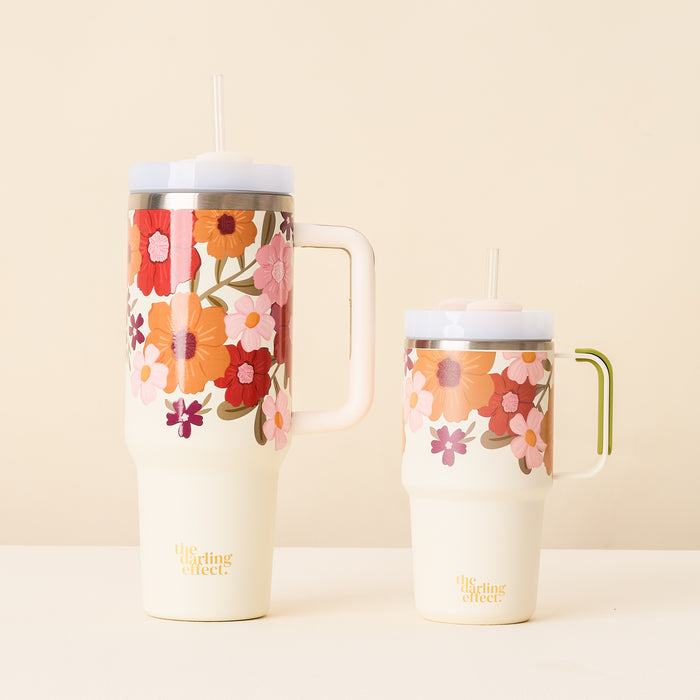 Two cream-colored Wild About You Cream 20 oz Mini On the-Go Tumblers by The Darling Effect, each with a handle, straw, colorful floral design, and "the darling effect" in gold near the bottom, are displayed side by side.