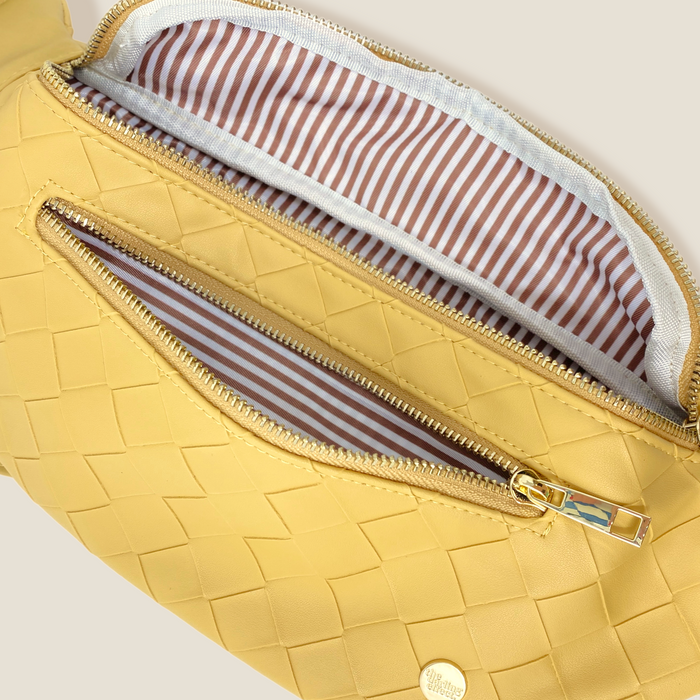 A close-up of The Darling Effect’s Woven Mustard Trendy Luxe Belt Bag reveals a zippered pocket, beige and white striped lining, and a gold zipper pull, blending hands-free style with chic woven design.