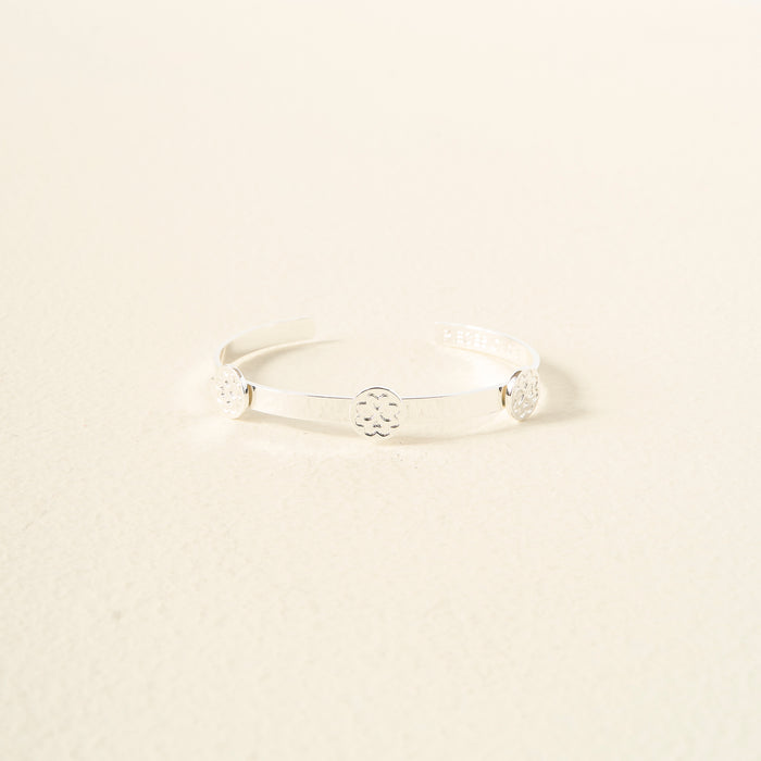 The Darling Effect's You Are Loving Skinny Stacker Bracelet—a minimalist silver adjustable cuff with three circular floral designs—is an elegant, gift-ready accessory styled on a light cream textured surface.