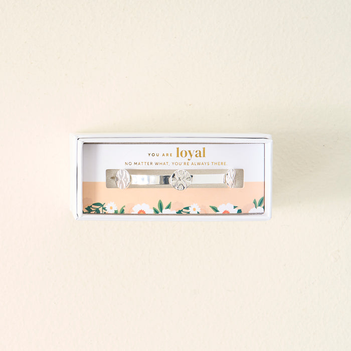 Gift-ready in a white box, The Darling Effect's "You Are Loyal" Skinny Stacker Trait Bracelet is a silver adjustable cuff with floral engravings. The lid reads, "YOU ARE loyal" and has a floral design at the bottom.