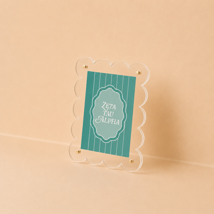 The Darling Effect’s Zeta Tau Alpha Mini Acrylic Picture Frame Magnet features scalloped edges and a teal card with white text, styled like a mini frame, and is shown propped against a neutral beige background.