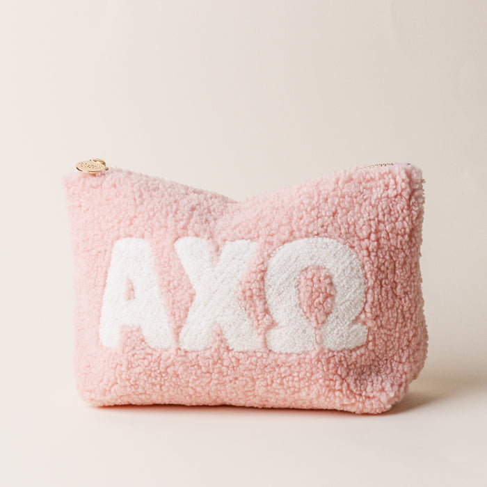 The Darling Effect’s Alpha Chi Omega Blush Teddy Letter Pouch features soft pink sherpa and white ΑΧΩ letters, making it a perfect carry-on accessory. Shown on a plain, light beige background.