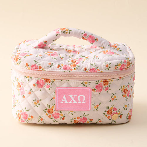 The Alpha Chi Omega Glam & Go Quilted Cosmetic Bag by The Darling Effect features a floral quilted design, a convenient handle, a pink zipper, and a pink patch with the Greek letters ΑΧΩ on the front—making this sorority cosmetic bag both stylish and functional for everyday use.