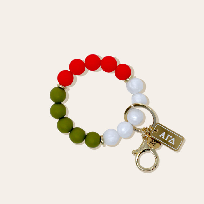 The Darling Effect's Alpha Gamma Delta Hands-Free Keychain Wristlet features red, green, and white beads, a gold keyring, lobster clasp, and Greek letter charm—perfect as a stylish sorority accessory.