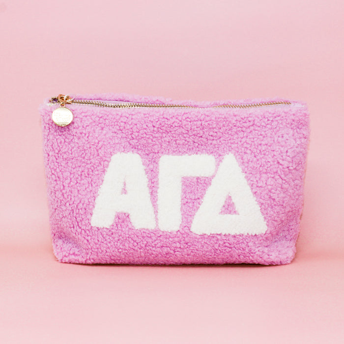 The Darling Effect Alpha Gamma Delta Lilac Teddy Letter Pouch features plush lilac fabric, white ΑΓΔ letters, and a gold zipper—perfect for organizing essentials or as a stylish accessory.