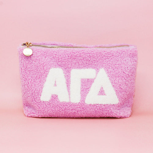 The Darling Effect Alpha Gamma Delta Lilac Teddy Letter Pouch features plush lilac fabric, white ΑΓΔ letters, and a gold zipper—perfect for organizing essentials or as a stylish accessory.