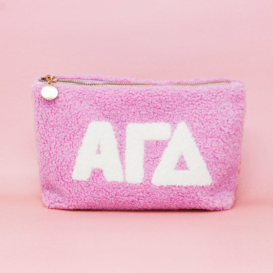 The Darling Effect Alpha Gamma Delta Lilac Teddy Letter Pouch features plush lilac fabric, white ΑΓΔ letters, and a gold zipper—perfect for organizing essentials or as a stylish accessory.