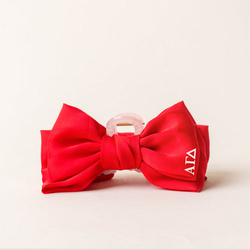 The Darling Effect Alpha Gamma Delta Satin Bow Claw Clip features a large red satin bow, clear clamp, and white ΑΓΔ Greek letters—ideal for updos.