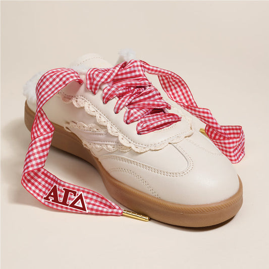 The Darling Effect’s Alpha Gamma Delta Step It Up Shoelaces, gold-tipped and printed with red ΑΓΔ letters on one tip, feature a chic red gingham print with lace trim—perfect for styling white sneakers with a tan sole.