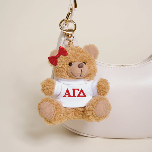 The Darling Effect’s Alpha Gamma Delta Teddy Bear Bag Charm features a red bow and a white shirt with red Greek letters, making it the perfect sorority gift or a stylish accessory for your handbag.
