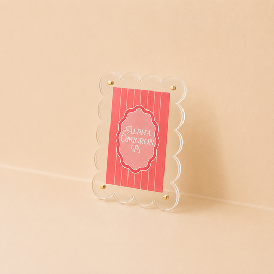The Darling Effect's Alpha Omicron Pi Mini Acrylic Picture Frame Magnet features a clear scalloped edge and gold screws, displaying a red Alpha Omicron Pi card—ideal for showcasing small prints or polaroid magnets.