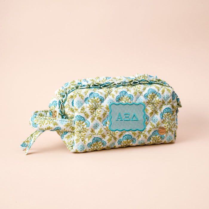 The Darling Effect Alpha Xi Delta Essentials Quilted Cosmetic Pouch features a floral quilted design, zipper, side handle, and a blue ΑΞΔ patch—perfect for sorority members. Shown on a beige background.
