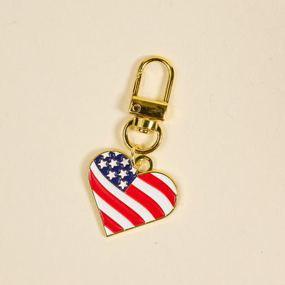 The Darling Effect's Americana Heart Pawfect Collar Charm is a gold keychain featuring a heart-shaped American flag design—perfect for adding patriotic flair and unique style to your pet’s collar.