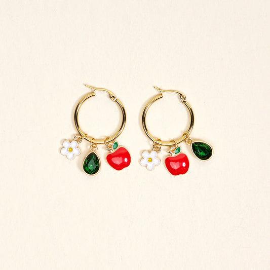 The Darling Effect’s Apple of My Eye Signature Hoop Earrings feature gold hoops with white flower, red apple, and green teardrop charms—playful jewelry for everyday wear, shown on a simple light background.