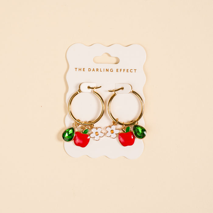 The Darling Effect's Apple of My Eye Signature Hoop Earrings feature gold hoops with red apple, green leaf, and white flower charms—playful accents to brighten up your everyday jewelry collection.