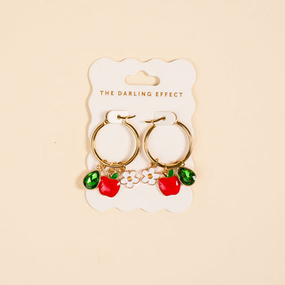 The Darling Effect's Apple of My Eye Signature Hoop Earrings feature gold hoops with red apple, green leaf, and white flower charms—playful accents to brighten up your everyday jewelry collection.