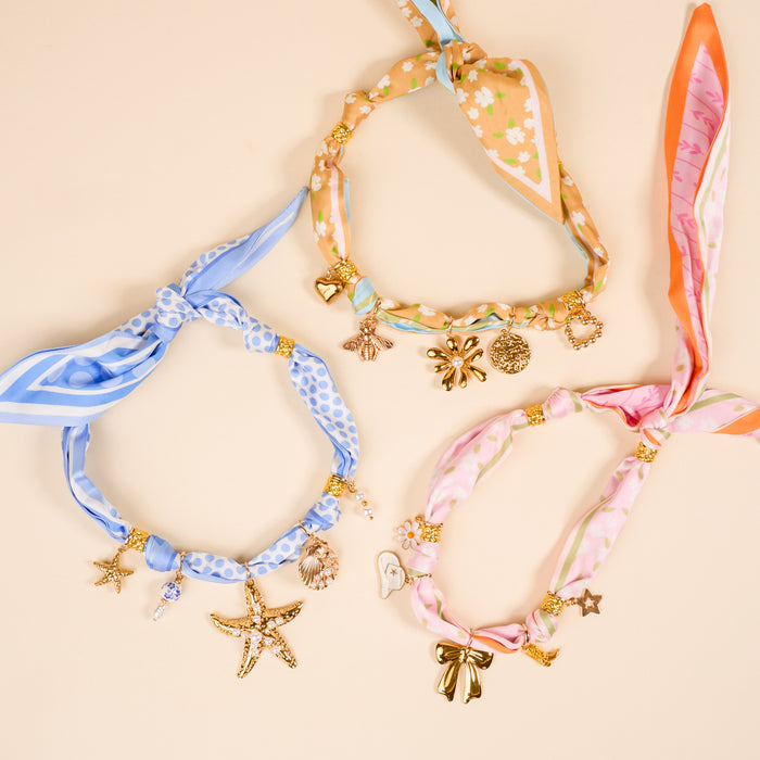 Three fabric necklaces from The Darling Effect’s Apple of My Eye Ultimate Charm Pack: blue polka dot and stripe with starfish and shell charms, peach floral with bee, flower, heart, and pink floral with bow, star, daisy charms.