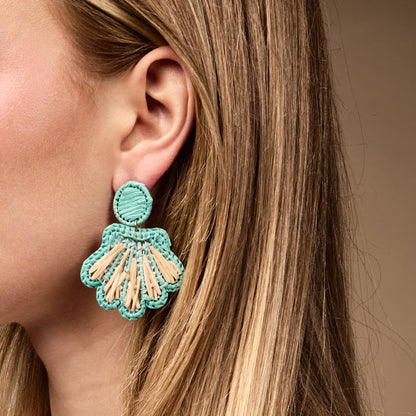 Close-up of a woman's ear wearing The Darling Effect's Aqua Cabana Breeze Earrings, large boho flower-shaped accessories in turquoise and beige. Ideal for daily wear, her straight light brown hair is partly shown.