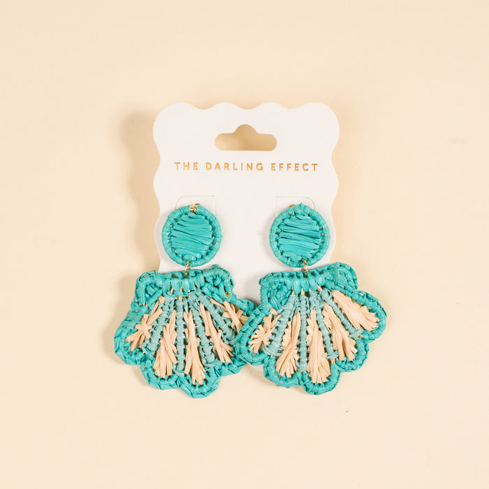 The Darling Effect's Aqua Cabana Breeze Earrings—turquoise and beige woven shells on a white card with the brand print—are lightweight, boho-chic accessories perfect for everyday style against a light beige backdrop.