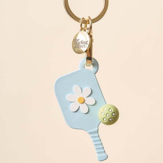 The Darling Effect's Aqua Pickleball Paddle Keychain features a pastel blue paddle with a white and yellow daisy, a green ball, and a gold charm—making it the perfect unique gift for pickleball lovers.