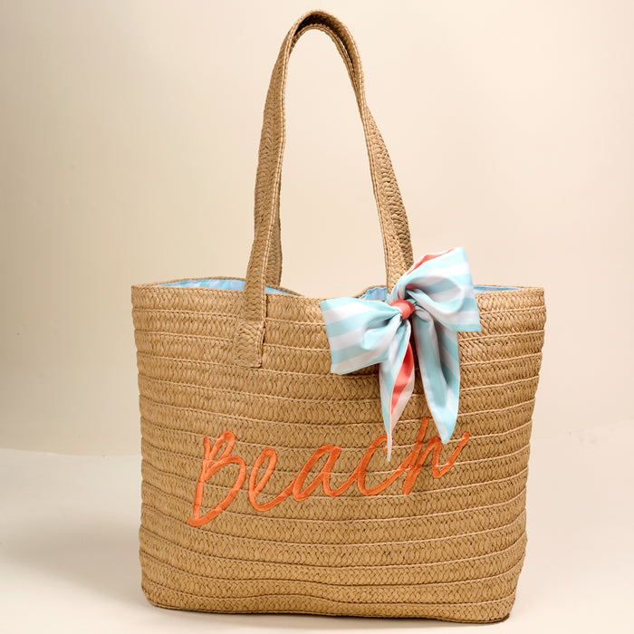 The Darling Effect Beach Straw & Sun Tote features "Beach" embroidered in orange and a large blue, white, and pink striped bow on one handle. This lightweight tote is displayed against a plain, light backdrop.