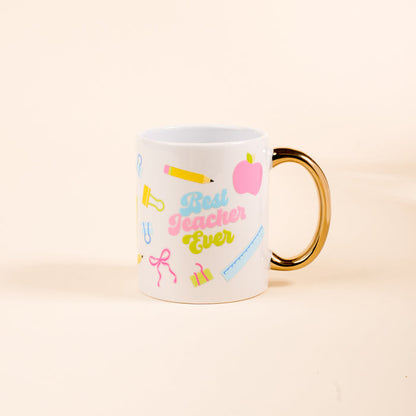 The Darling Effect's Best Teacher Ever 11 oz Cozy Cute Ceramic Mug features a gold handle and school-themed icons—a pink apple, yellow pencil, and ruler—making it the perfect gift for teachers to enjoy coffee or tea.