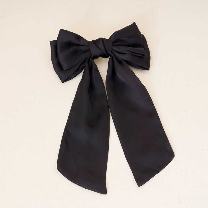 The Darling Effect’s Black Satin Hair Bow, featuring two long tails, is displayed on a light background—an elegant addition to any hair accessories collection.