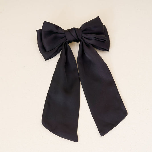 The Darling Effect’s Black Satin Hair Bow, featuring two long tails, is displayed on a light background—an elegant addition to any hair accessories collection.
