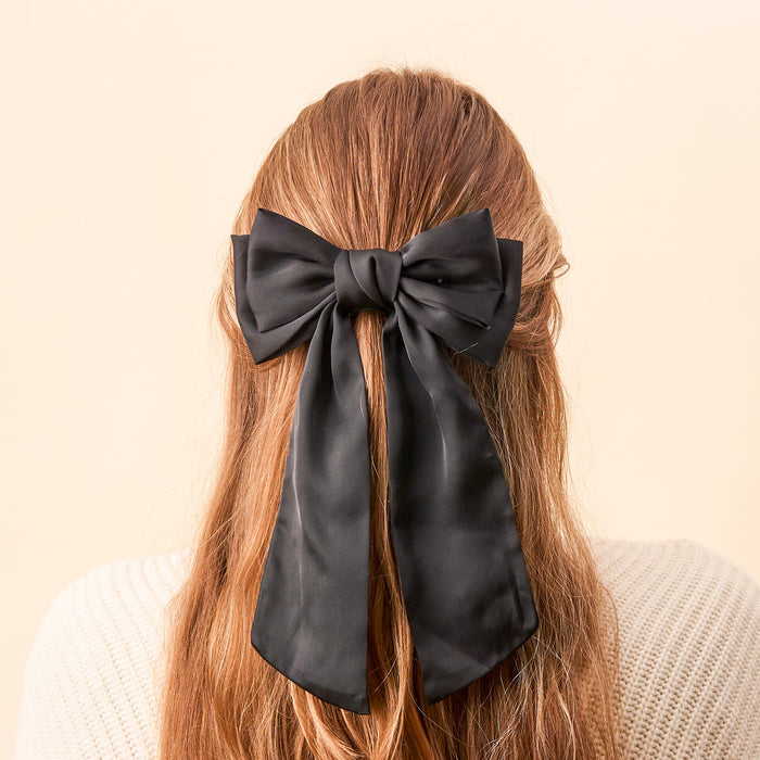 Back view of a person with long, light brown hair styled in The Darling Effect’s Black Satin Hair Bow, paired with a cream sweater for an effortlessly elegant look that highlights chic hair accessories.
