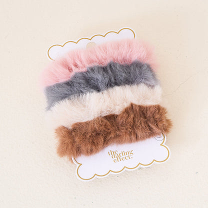 The Darling Effect’s Bliss Faux Fur Scrunchie Set features four soft scrunchies in pink, gray, cream, and brown—luxurious accessories to elevate your hair collection.